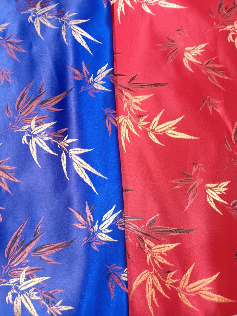 May include: Close-up of two fabric panels, one blue and one red. Both panels feature a repeating pattern of bamboo leaves in gold and brown. The fabric has a slight sheen, suggesting a satin or silk material.