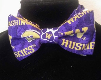 Może przedstawiać: Fioletowy i złoty krawat w kształcie muszki z logo Washington Huskies i nadrukiem słów "Washington Huskies" i "Skies".