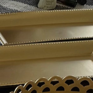 May include: Two gold-colored rectangular trays with beaded edges. The trays are stacked on top of each other.