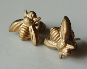 May include: A pair of gold bee-shaped stud earrings. The bees are detailed with textured wings and bodies.