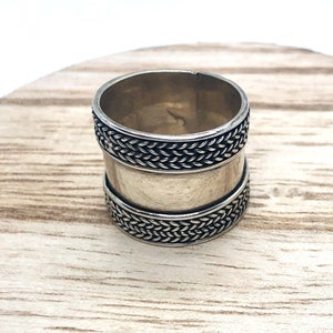 May include: A silver ring with a braided design around the band.