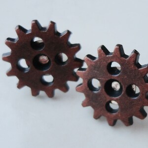 May include: A pair of copper-colored metal gear earrings. The gears have a black center and are detailed with small holes around the edges.