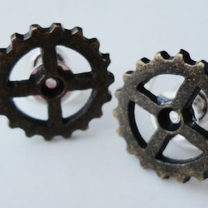 May include: A pair of bronze-colored metal gear earrings. Each earring features a detailed gear design with a silver post.