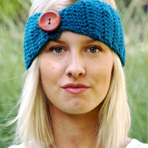 May include: A teal blue crocheted headband with a brown wooden button. The headband is worn by a person with blonde hair.