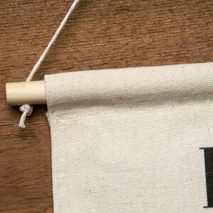 May include: A white canvas banner with the word "boho" printed in black. The banner is hanging from a wooden dowel rod with a white string.