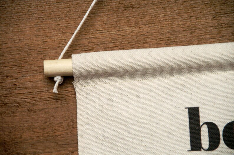 May include: A white canvas banner with the word "boho" printed in black. The banner is hanging from a wooden dowel rod with a white string.