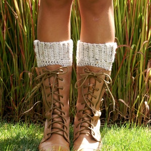 May include: Brown leather lace-up boots with white crocheted leg warmers. The boots are worn by a person standing in tall grass.