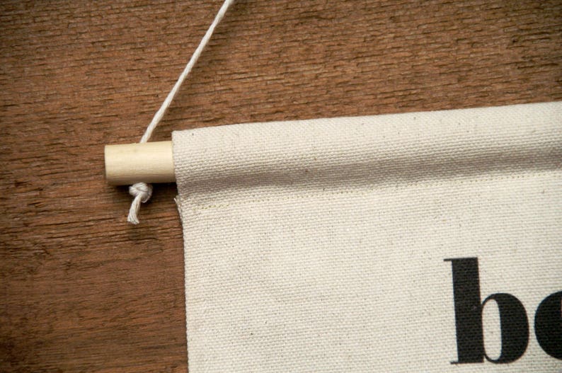 K&ouml;nnte beinhalten: Ein wei&szlig;es Canvas-Banner mit dem Wort "boho" in Schwarz gedruckt. Das Banner h&auml;ngt an einer Holzleiste mit einer wei&szlig;en Schnur.