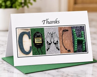 May include: A white greeting card with the word Thanks printed above a rectangular graphic spelling COACH. The letters are formed by a dark letter C, a black digital stopwatch, two winged running shoes, a black lanyard, and a green letter H.