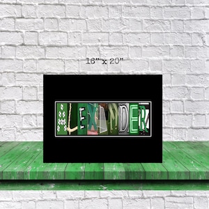 Op de afbeelding: Een zwart ingelijst afdruk met de naam "ALEXANDER" gespeld in groene en witte letters. Elke letter is gemaakt van afbeeldingen die te maken hebben met voetbal.