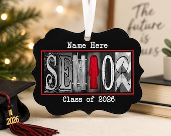 May include: A black scalloped-edge ornament featuring a white ribbon hanger. The text "Name Here" appears at the top, "Class of 2026" at the bottom, and the word "SENIOR" in the center, with a red graduation gown replacing the letter "I".