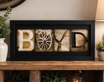 May include: A rectangular black frame containing four square panels that spell the name BOYD. The first panel shows the letter B, the second a wagon wheel, the third a tree branch, and the fourth the letter D, all in sepia tones.