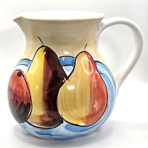 May include: A ceramic jug with a cream-coloured body and a white handle. The jug is decorated with colourful painted pears in shades of yellow, red, and brown, set against a blue and white background. The jug has a spout for pouring.