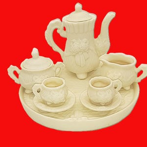 May include: Cream-colored ceramic tea set with a teapot, sugar bowl, creamer, two teacups, and saucers, all on a matching tray. The teapot features a floral design. The set is ideal for a tea party.