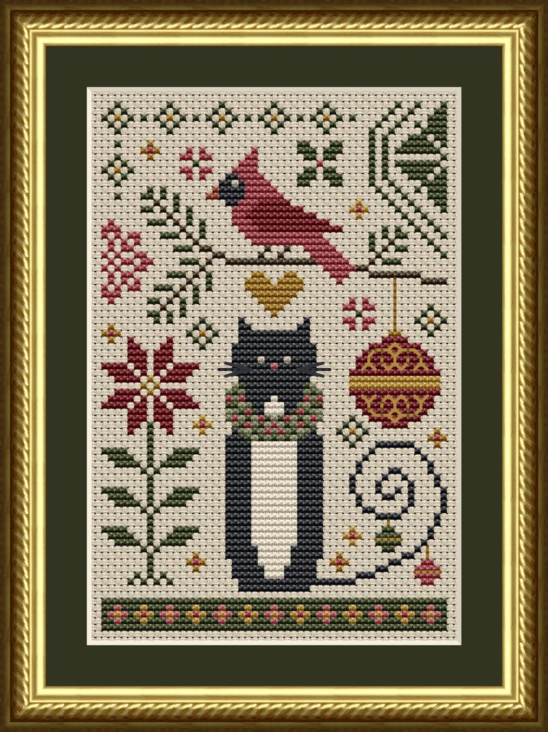 May include: A cross-stitch embroidery featuring a black cat wearing a wreath, a red cardinal on a branch, a gold heart, a red and gold ornament, and a poinsettia flower. The design is set against a cream-coloured fabric background and framed.