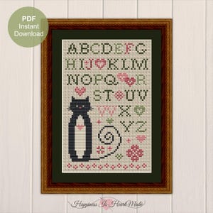 以下が含まれることがあります： 黒い猫が白い胸と丸まった尻尾でクロスステッチの模様になっています。猫はピンクのハートと緑の葉のあるカラフルなアルファベットで囲まれています。パターンは茶色の木製のフレームで囲まれています。フレームの下に「Happiness Is Heart Made」というテキストが印刷されています。