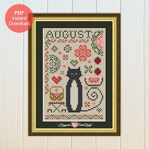May include: A cross-stitch pattern in a gold frame featuring the text AUGUST, a black cat with a white chest, a red heart, a picnic basket, a slice of watermelon, ladybugs, and floral motifs on a light fabric background with a black border.