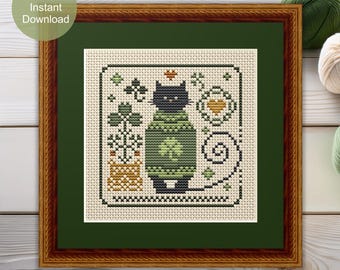 Könnte beinhalten: Ein Kreuzstichmuster mit einer schwarzen Katze, die einen grünen Pullover mit Kleeblattmuster trägt. Die Katze ist von dekorativen Elementen umgeben, darunter eine Topfpflanze mit Kleeblättern, ein Herz und Wirbelmuster auf cremefarbenem Stoff.