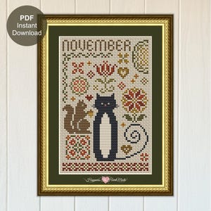 May include: Cross-stitch art in a gold frame featuring the word "NOVEMBER" at the top. The design includes a black cat, a squirrel, and floral patterns in red, brown, and green. The words "PDF Instant Download" are in a circle in the upper left corner.