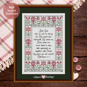 Könnte beinhalten: Gerahmtes Kreuzstich-Kunstwerk mit dunkelgrünem Passepartout und Holzrahmen. Das Design zeigt einen floralen Rand in Rot und Grün, der ein Zitat aus Epheser 2:4-5 umgibt. Der Text lautet "Aber Gott..." in schwarzer Schrift.