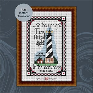 Pode incluir: Um padrão de ponto cruz com um farol às riscas pretas e brancas, um pequeno edifício vermelho e o texto Unto the upright There Ariseth light in the darkness Psalm 112:4 Cape Hatteras. O design está numa moldura de madeira escura.