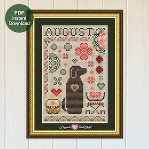 May include: A cross-stitch pattern featuring the word AUGUST in black letters, a central brown dog silhouette with a heart, red ladybugs, a watermelon slice, a basket, and floral motifs in red and green on a light fabric background in a gold frame.