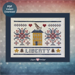 Op de afbeelding: Een kruissteekpatroon met een centraal geel huis met een vogel op het dak, geflankeerd door twee grote rood-blauwe bloemmotieven. Het ontwerp bevat het woord LIBERTY in het blauw, geaccentueerd door gele sterren en bruine klokken op witte stof.