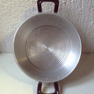 May include: A silver colander with two brown handles. The colander has a round shape and a perforated bottom.