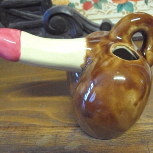 Peut inclure: Une figurine en céramique brune en forme de corps humain. La figurine a une tête blanche et rose et un corps brun avec une poignée au dos.