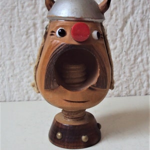 Könnte beinhalten: Ein Nussknacker aus Holz in Form eines Wikingerkopfes. Der Nussknacker hat einen silbernen Helm, eine rote Nase und einen großen Mund mit einem Schraubmechanismus zum Knacken von Nüssen.