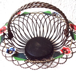 May include: A wire basket with a brown metal frame and a black base. The basket is decorated with colourful flowers and leaves.