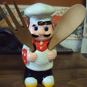 Peut inclure: Une figurine de chef en céramique avec un chapeau de chef blanc, un tablier à pois rouges et blancs et des yeux bleus. Le chef tient deux ustensiles en bois, une cuillère et une fourchette.