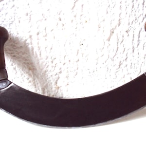 May include: A curved, metal butcher knife with two wooden handles. The knife has a dark, aged finish and is designed for cutting meat.