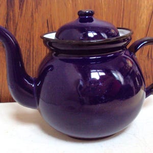May include: A deep purple enamel teapot with a white rim and a black handle. The teapot has a round body and a classic design.