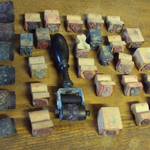 May include: A collection of vintage wooden printing blocks with various designs and a hand-crank printing press. The blocks are arranged on a wooden surface and feature a variety of patterns and letters.