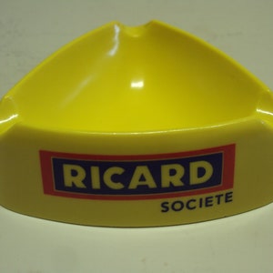 Peut inclure: Cendrier triangulaire jaune avec le texte "RICARD SOCIETE" imprimé sur le devant.
