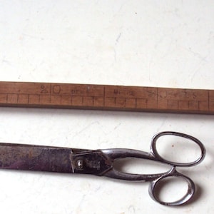 Może przedstawiać: Drewniana linijka z oznaczeniami do 40 cali i srebrne nożyczki.