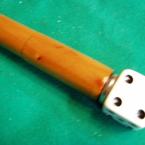 May include: A wooden pen with a white dice attached to the end. The dice has black dots on each side.