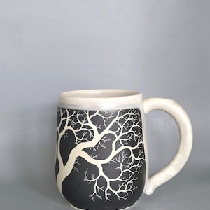 Auf dem Rad geworfener Sgraffito-Steingutbecher - geätzter Winterbaum in mattem Schwarz mit gesprenkelter Sahneglasur - handgemachte schlammige Rabenkeramik