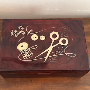 May include: A rectangular dark brown marbled sewing box with a hinged lid. The top features gold-colored etched illustrations of scissors, a spool of thread, buttons, and a needle, with the text "For my Sewing" written in a cursive script.