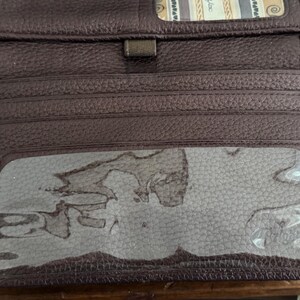 May include: A dark brown textured leather wallet featuring multiple horizontal card slots, a central rectangular clear plastic ID window, and a small top compartment with a patterned fabric lining visible at the upper edge of the open interior.