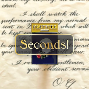 Puede incluir: Un pin de esmalte azul y dorado con un programa de teatro con el texto "PLAYBILL" y las palabras "Seconds!" en una pancarta blanca. El pin también presenta una máscara blanca con una rosa roja.