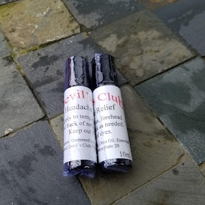May include: Two small, cylindrical bottles with black caps and white labels. One reads "evil Headache" and the other "Club Relief" in red text. The bottles are on a stone surface.