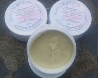 Könnte beinhalten: Drei weiße Tiegel Brustbalsam mit der Aufschrift "Devil's Club Just Breathe" und "Chest Rub". Einer ist geöffnet und zeigt einen hellgelben Balsam. Die Etiketten listen Bio-Zutaten auf und sind 42.5g.
