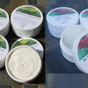 May include: Several white plastic jars of face cream with circular labels. The labels feature green or red botanical imagery and text including Devil's Club Anti-Aging Face Cream or Day Time Devil's Club Anti-Aging Cream with Frankincense, 1.5oz, SPF 15.