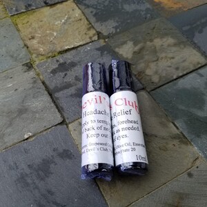 K&ouml;nnte beinhalten: Zwei kleine, zylindrische Flaschen mit schwarzen Kappen und wei&szlig;en Etiketten. Auf einer steht "evil Headache" und auf der anderen "Club Relief" in roter Schrift. Die Flaschen stehen auf einer Steinoberfl&auml;che.
