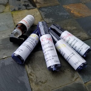 K&ouml;nnte beinhalten: Mehrere kleine, zylindrische Flaschen mit wei&szlig;en Etiketten und schwarzen Kappen liegen auf einer Steinoberfl&auml;che. Die Etiketten tragen die Aufschrift "Club Relief" und "Allergy Relief". Die Flaschen enthalten &auml;therische &Ouml;le, Volumen 10 ml.