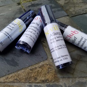 K&ouml;nnte beinhalten: Vier Roll-on-Flaschen mit wei&szlig;en Etiketten und dunkelblauen Kappen. Die Etiketten tragen Texte wie "Relief Club" und "Devil's Allergy". Jede Flasche enth&auml;lt 10 ml.