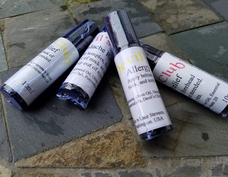 K&ouml;nnte beinhalten: Vier Roll-on-Flaschen mit wei&szlig;en Etiketten und dunkelblauen Kappen. Die Etiketten tragen Texte wie "Relief Club" und "Devil's Allergy". Jede Flasche enth&auml;lt 10 ml.