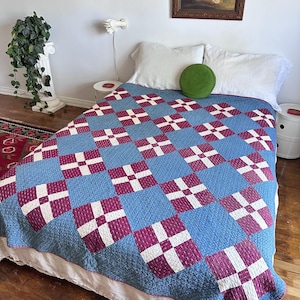 May include: A bed quilt featuring a repeating patchwork pattern of blue, magenta, and white squares. The blue squares have a subtle textured grid design, while the magenta squares feature a small white floral print. The quilt has a thin border.
